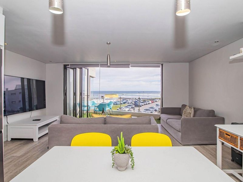 Modern open-plan living area featuring laminate flooring, recessed lighting, and large bi-fold doors opening to a balcony with coastal views.