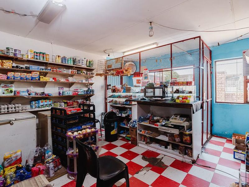A utility space or small shop area featuring fixed shelving, security mesh partitioning, and checkered tiled flooring in need of maintenance.