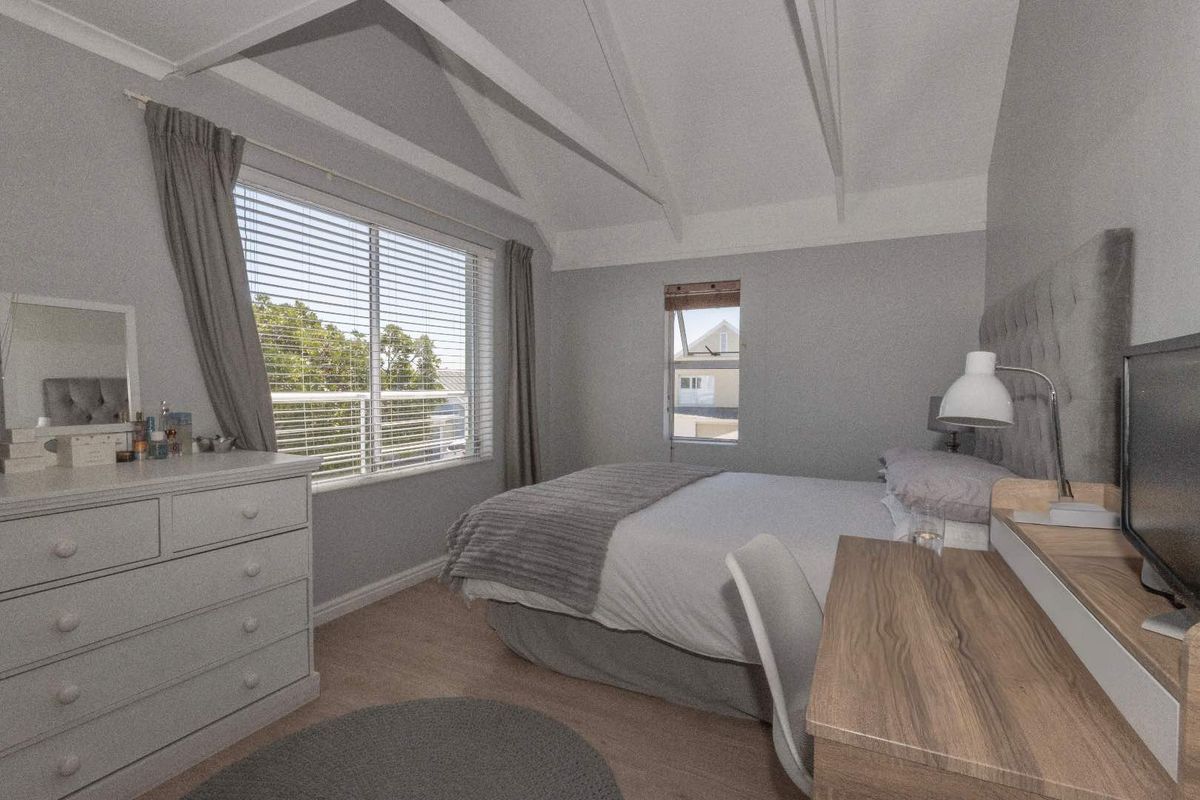 A well-maintained bedroom featuring a vaulted ceiling with exposed beams, laminate flooring, and large windows with venetian blinds.