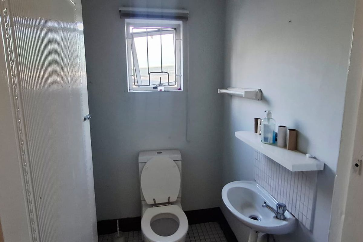 A compact, functional bathroom featuring a pedestal basin, toilet, and tiled flooring, requiring cosmetic updates to improve its overall condition and appeal.