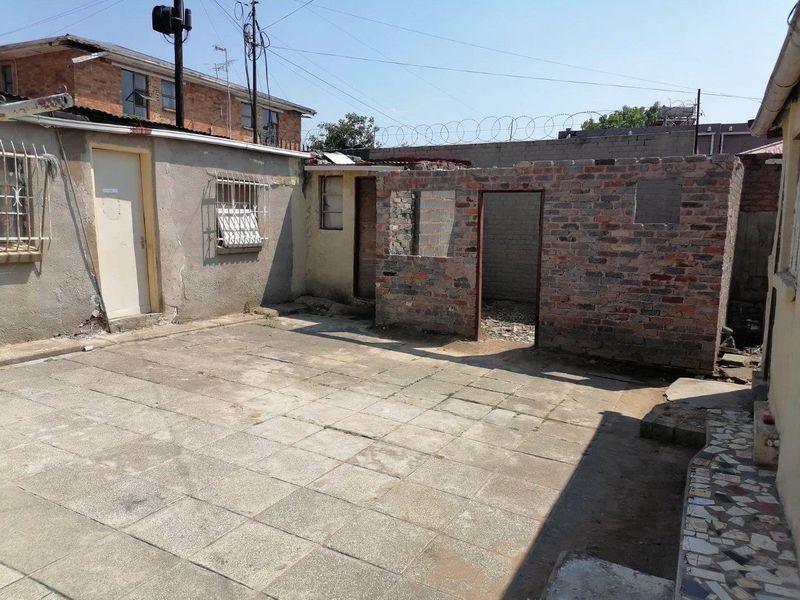 Rear courtyard area featuring paved flooring and unfinished brick structures, requiring significant maintenance and renovation to improve the exterior space.