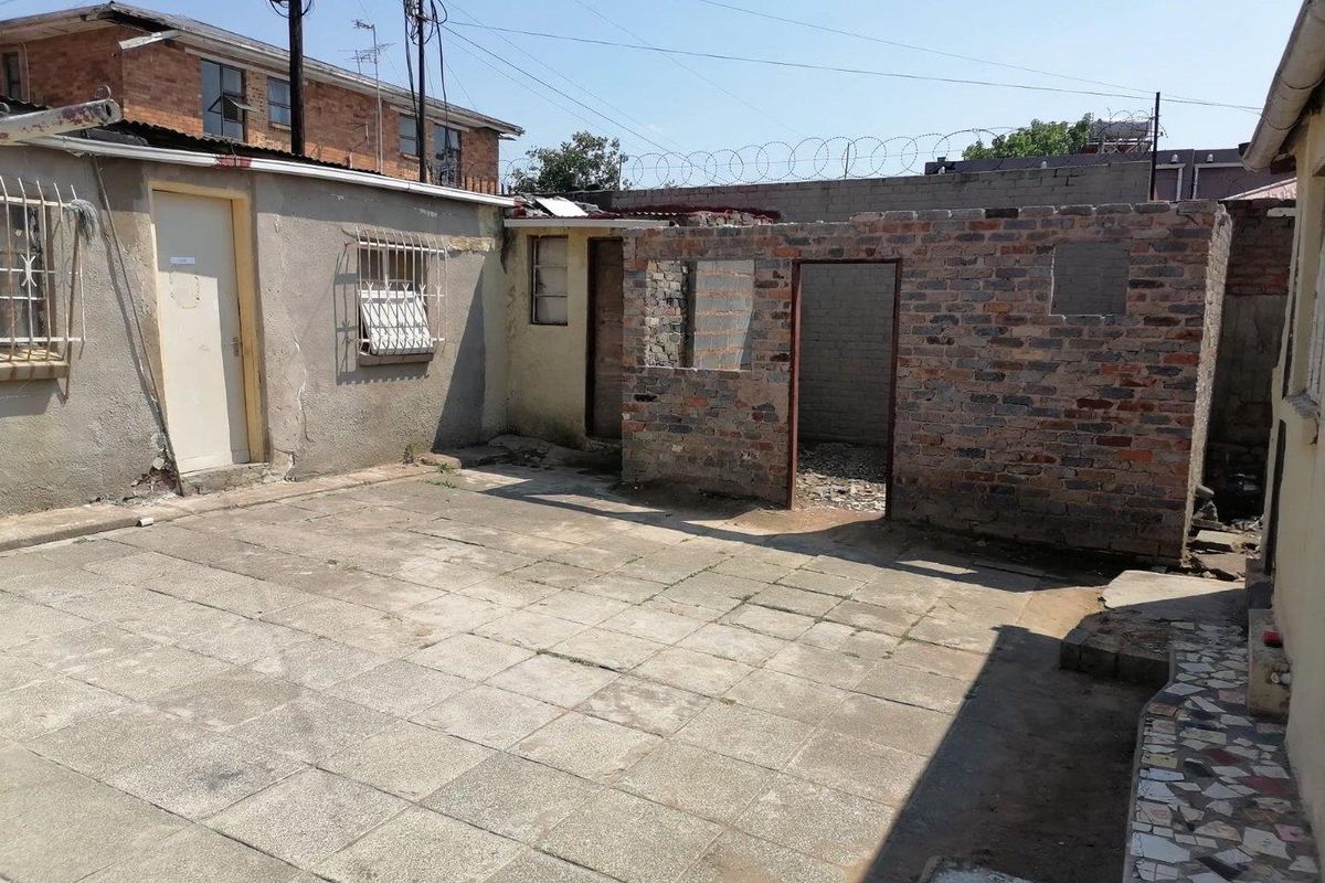 Rear courtyard area featuring paved flooring and unfinished brick structures, requiring significant maintenance and renovation to improve the exterior space.