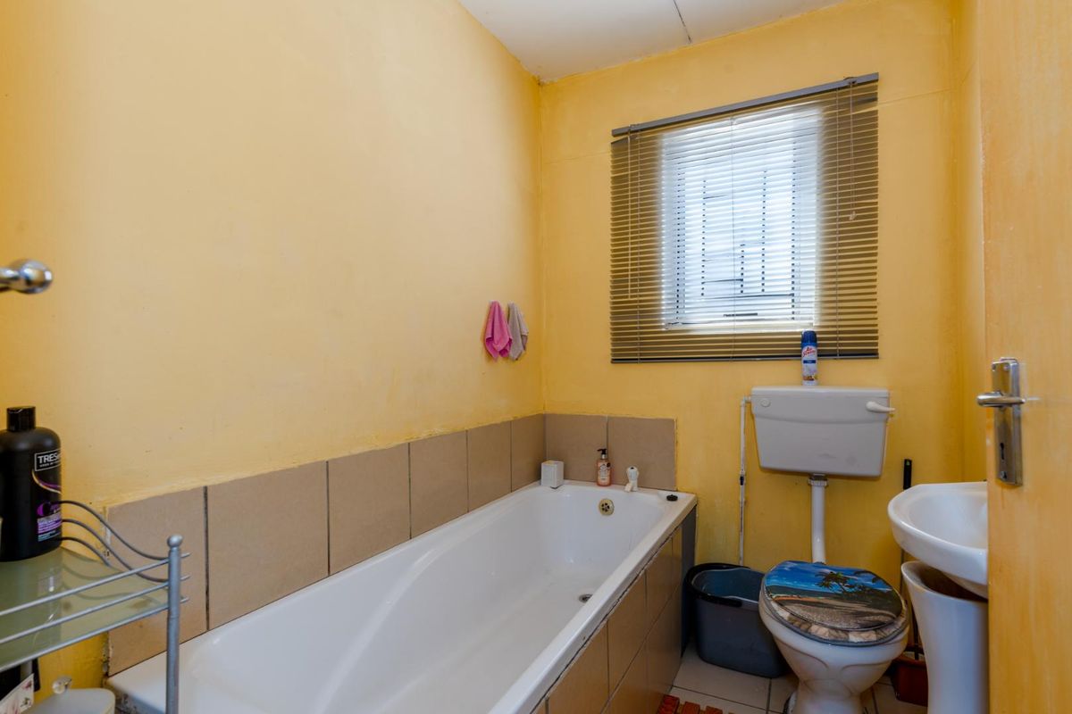 A compact bathroom featuring a standard bathtub, pedestal basin, and toilet, finished with yellow wall paint and neutral tiling.