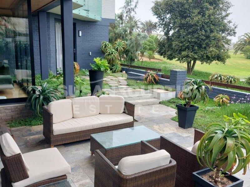 A covered patio featuring stone flooring and a timber ceiling, overlooking a landscaped garden and green space.