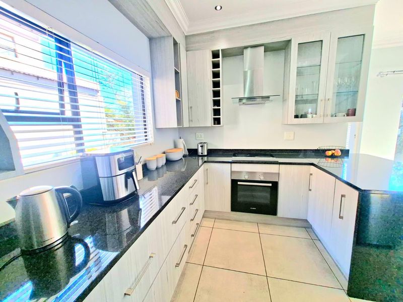 Modern kitchen featuring light wood-grain cabinetry, dark granite countertops, built-in oven, electric hob, and stainless steel extractor fan with tiled flooring.
