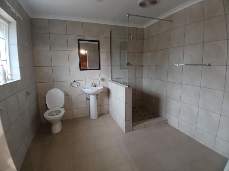 A clean, neutral-toned bathroom featuring a pedestal basin, toilet, and a spacious walk-in shower with a glass screen and tiled finishes.