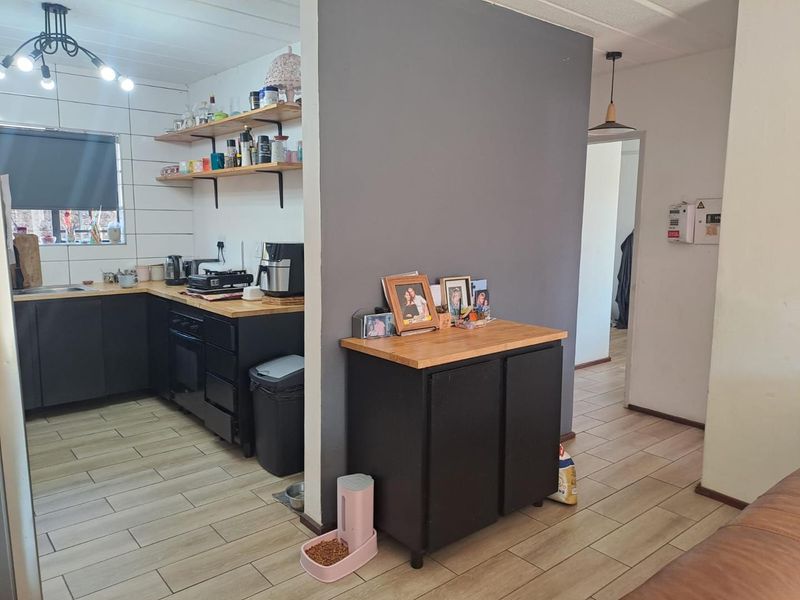Open plan kitchen area featuring dark cabinetry, wooden countertops, tiled flooring, and open shelving, seamlessly connecting to the adjacent living space.