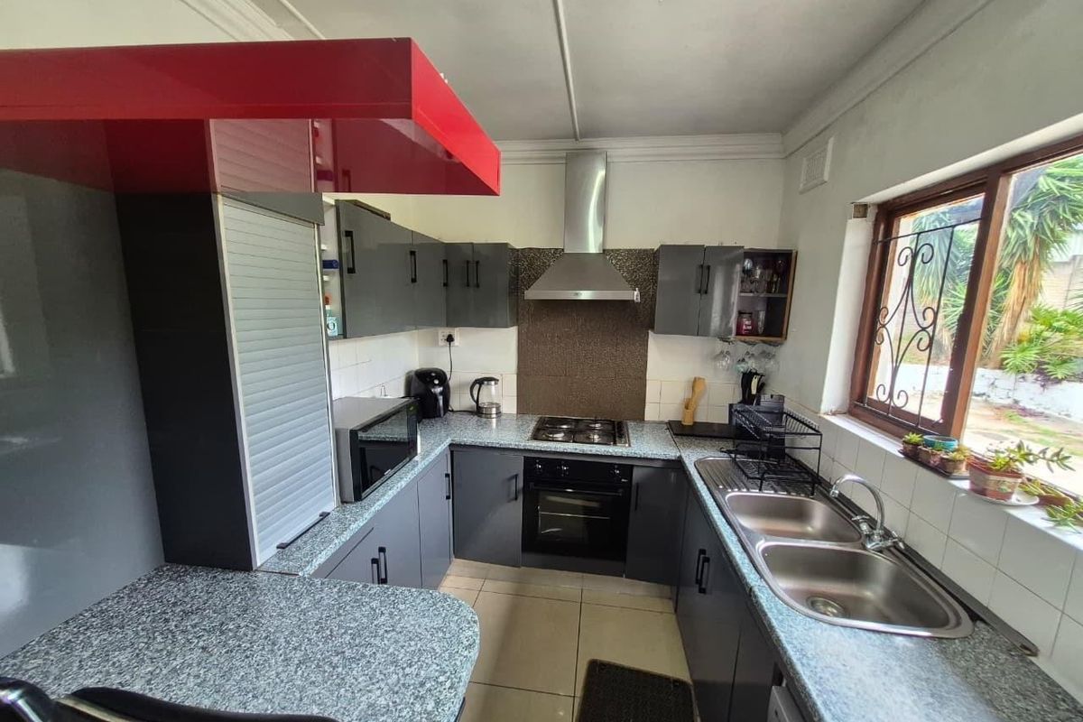Functional kitchen featuring grey cabinetry, laminate countertops, stainless steel double sink, built-in oven, and gas hob with extractor fan.