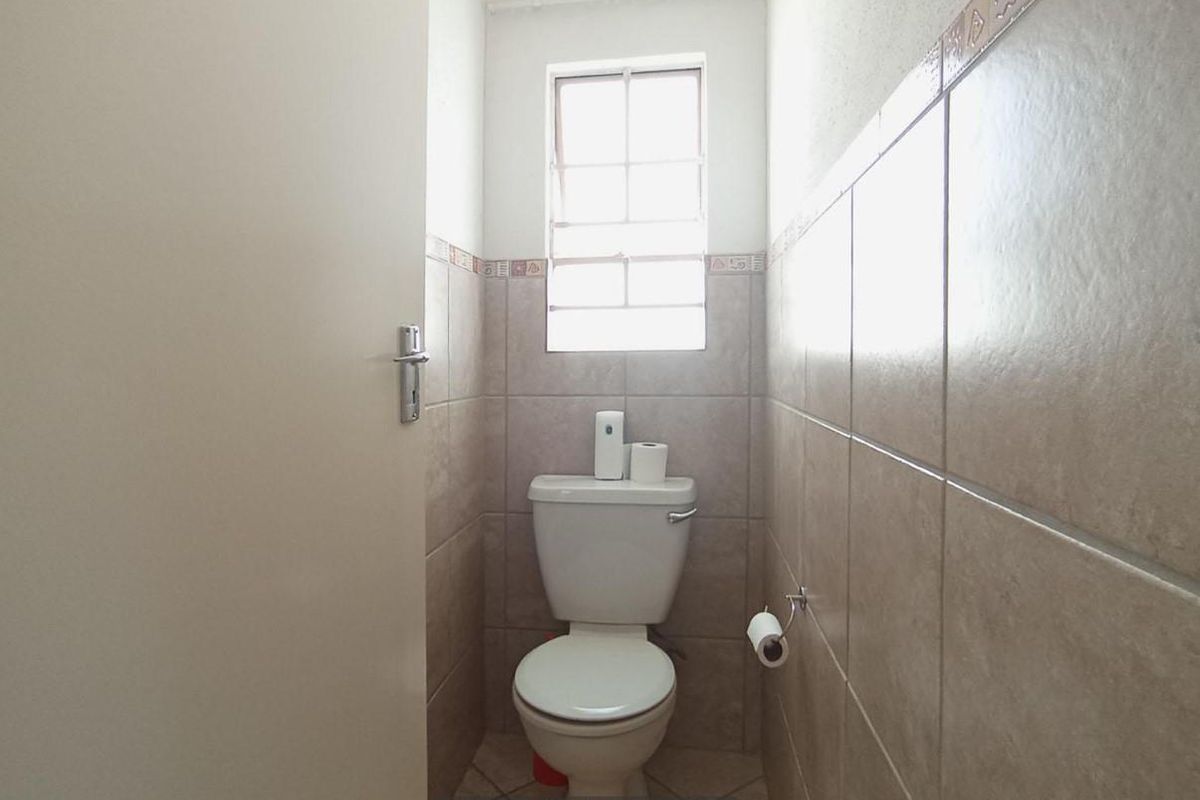 A compact guest bathroom featuring neutral wall tiling, a standard toilet, and a small window for natural light.