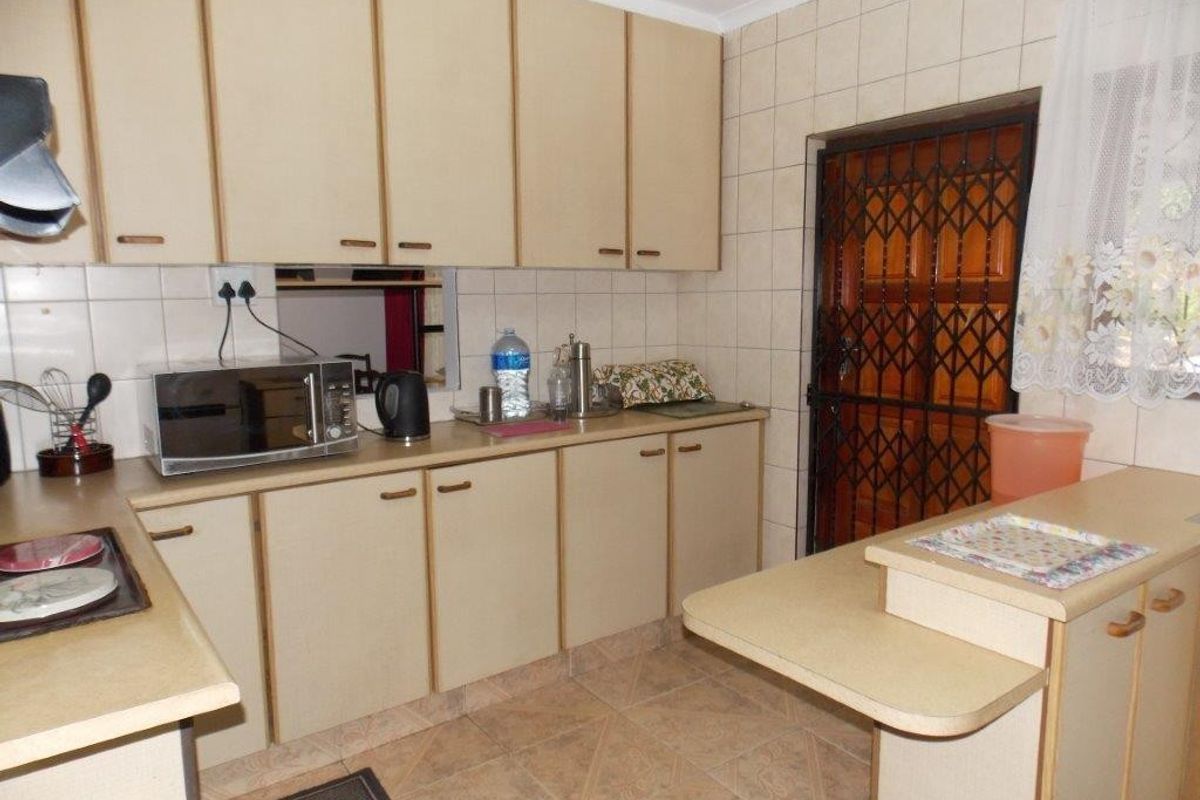 A functional kitchen featuring laminate cabinetry, tiled backsplash, and a breakfast nook, with direct access to the exterior via a security gate.