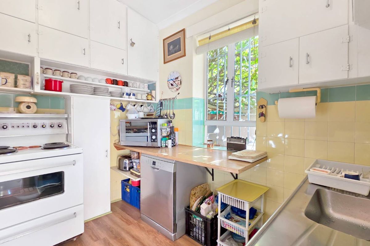 A compact, dated kitchen featuring original cabinetry, tiled splashbacks, and a functional layout with a stainless steel sink and freestanding stove.