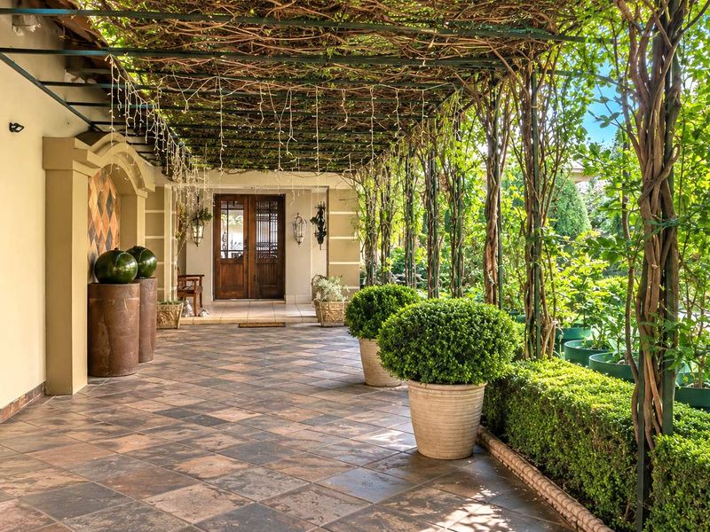 A spacious covered patio featuring tiled flooring, a vine-covered pergola, and elegant double wooden entrance doors, creating a charming outdoor transition area.