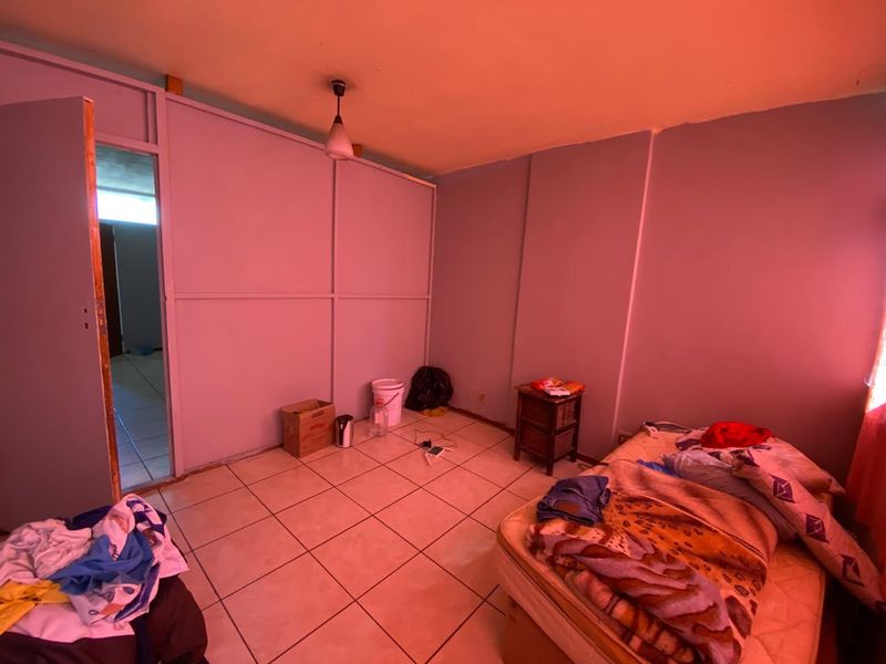 A bedroom featuring ceramic floor tiles and a partition wall, currently requiring cosmetic updates and improved lighting to enhance the living space.