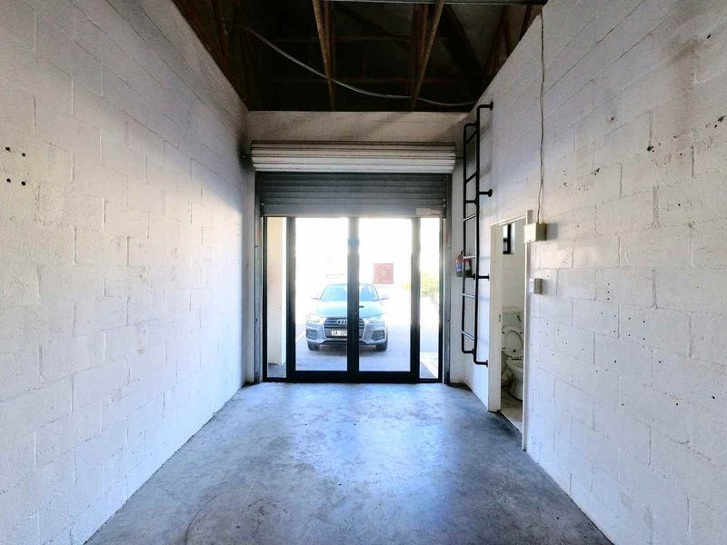 Industrial utility space featuring exposed roof trusses, concrete flooring, a roller shutter door, and an integrated toilet facility.