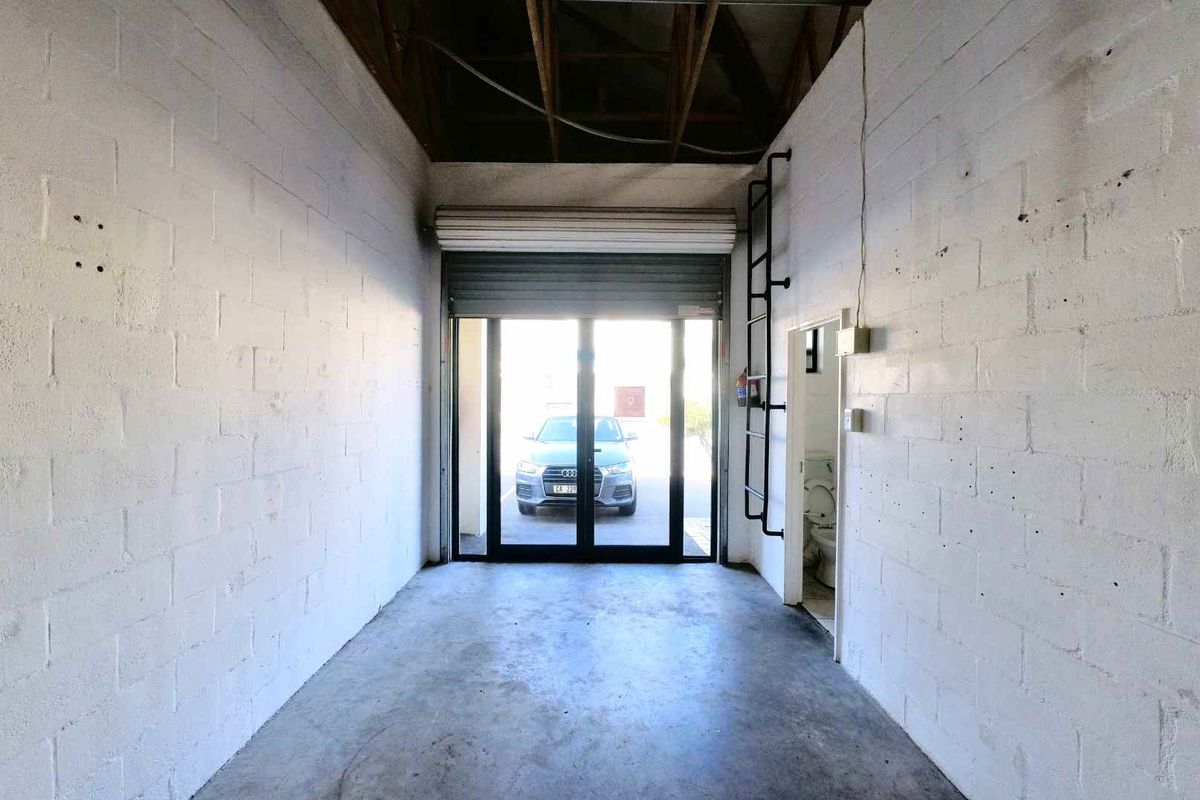 Industrial utility space featuring exposed roof trusses, concrete flooring, a roller shutter door, and an integrated toilet facility.
