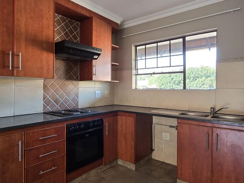 A functional kitchen featuring wooden cabinetry, built-in oven with hob, extractor fan, and a double basin sink with tiled backsplash.