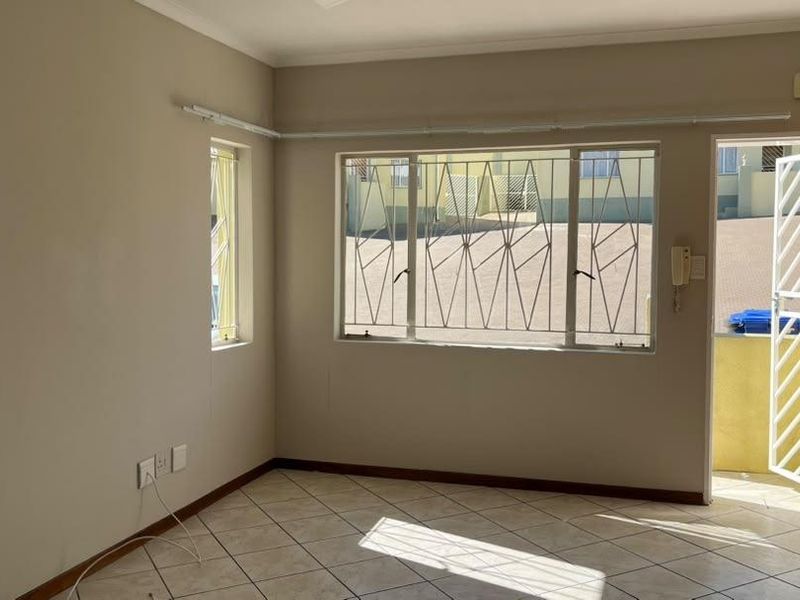 An empty living room featuring tiled flooring, security bars on windows, and a security gate leading to the exterior.