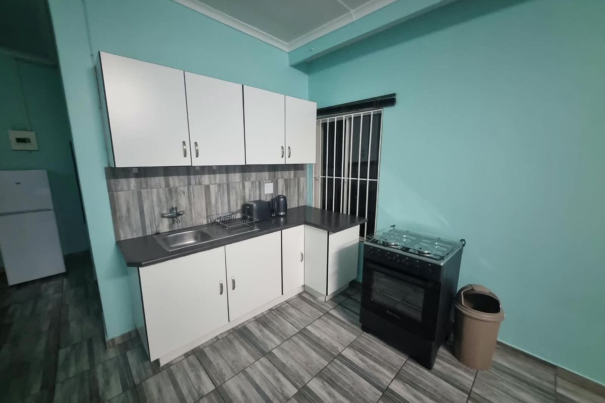 A functional kitchen featuring white cabinetry, dark laminate countertops, tiled backsplash, and tiled flooring, equipped with a freestanding stove and security bars on the window.