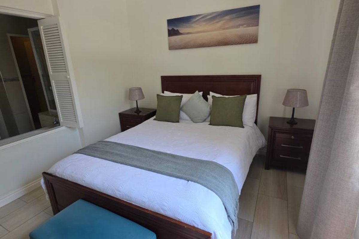A well-maintained bedroom featuring light-toned tiled flooring, crown molding, and a unique shutter window opening into an adjacent space.