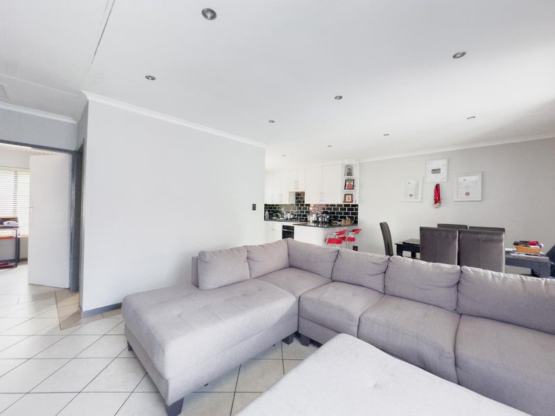 Open-plan living and dining area featuring tiled floors, recessed lighting, and a modern kitchen with white cabinetry and a dark subway tile backsplash.