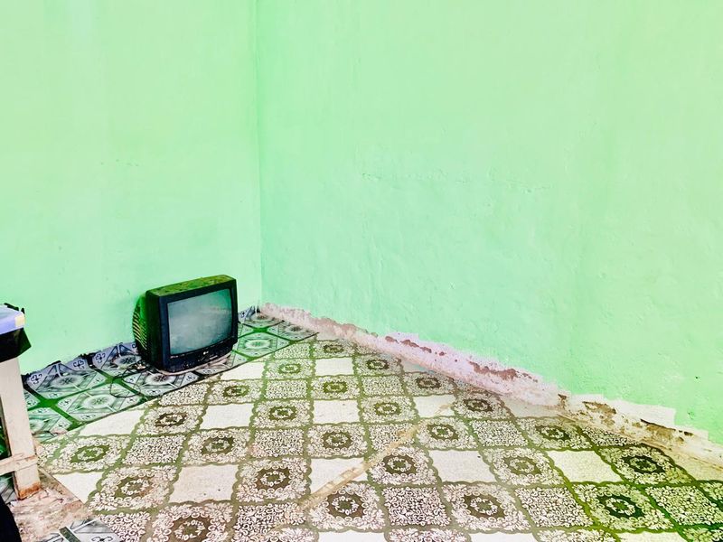 A sparse living area featuring patterned floor tiles and green walls showing signs of wear and moisture damage.