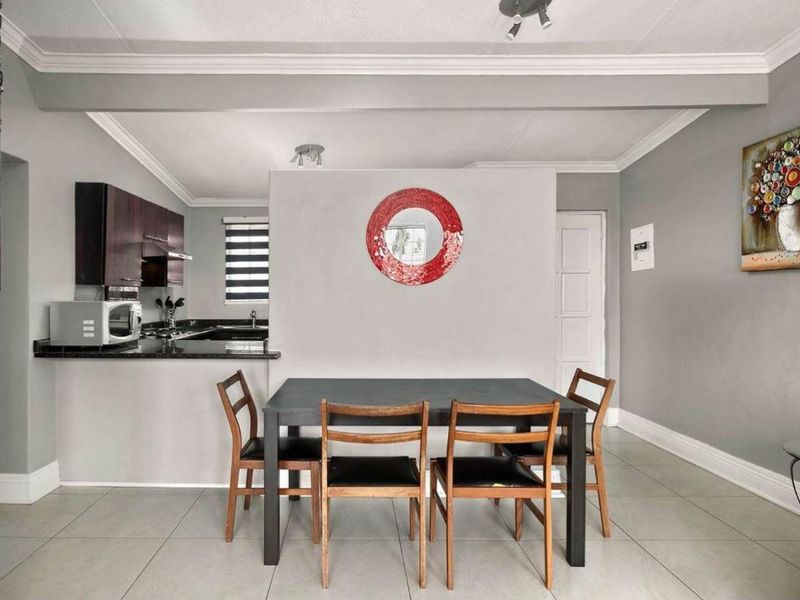 Open-plan living and dining area featuring a modern kitchen with dark cabinetry, granite countertops, and neutral tiled flooring throughout.
