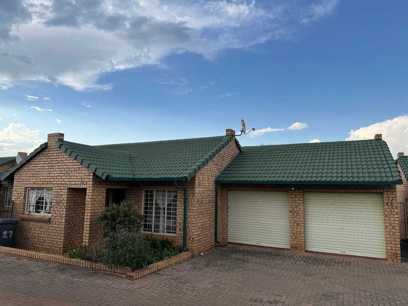 Front elevation of a face brick townhouse featuring a green tiled roof, double garage with roll-up doors, and a paved driveway.