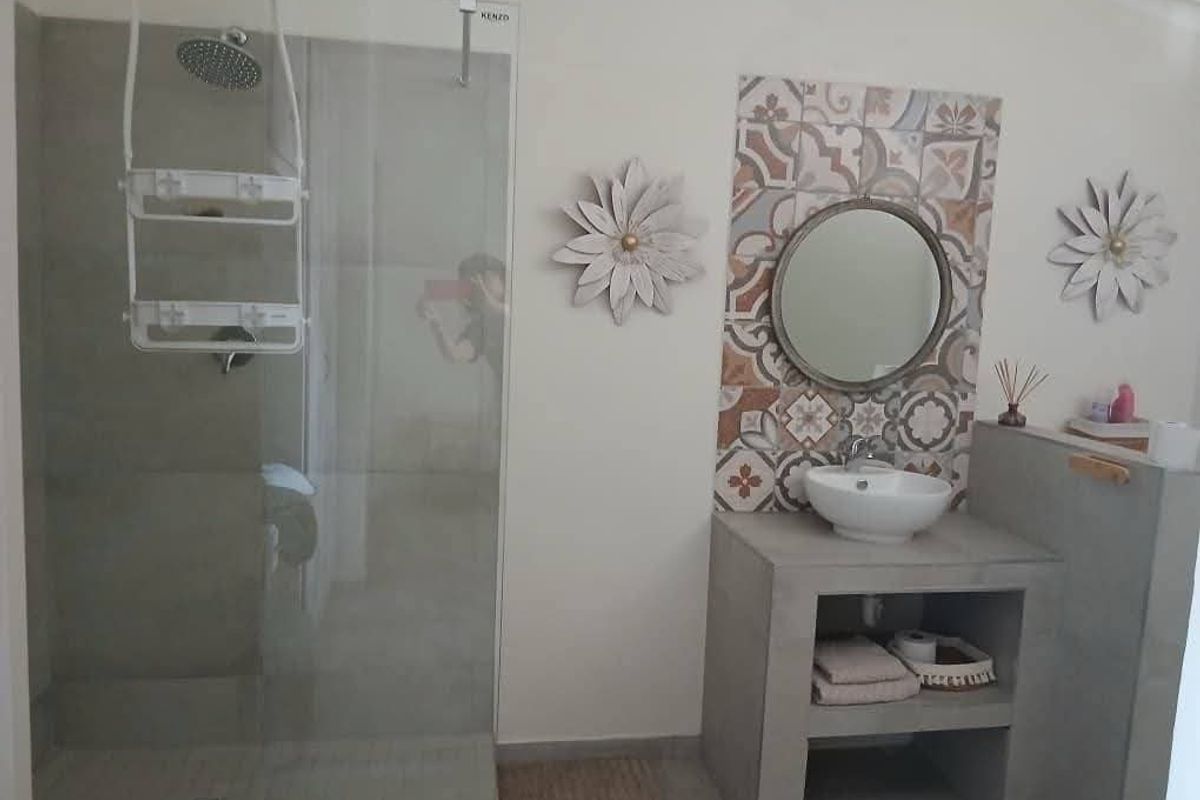 Modern bathroom featuring a walk-in shower with glass screen, concrete vanity with vessel sink, and decorative accent tiling.