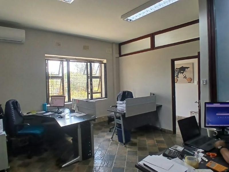 A functional office space featuring tiled flooring, split-system air conditioning, and large windows with security bars, providing a practical work environment.