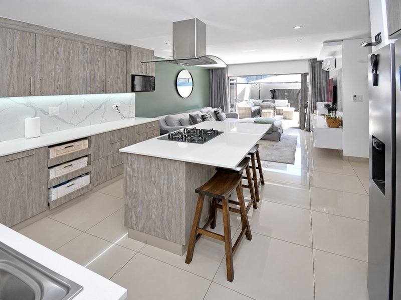 Modern open-plan kitchen and living area featuring a central island with gas hob, quartz countertops, and seamless flow to the outdoor patio.