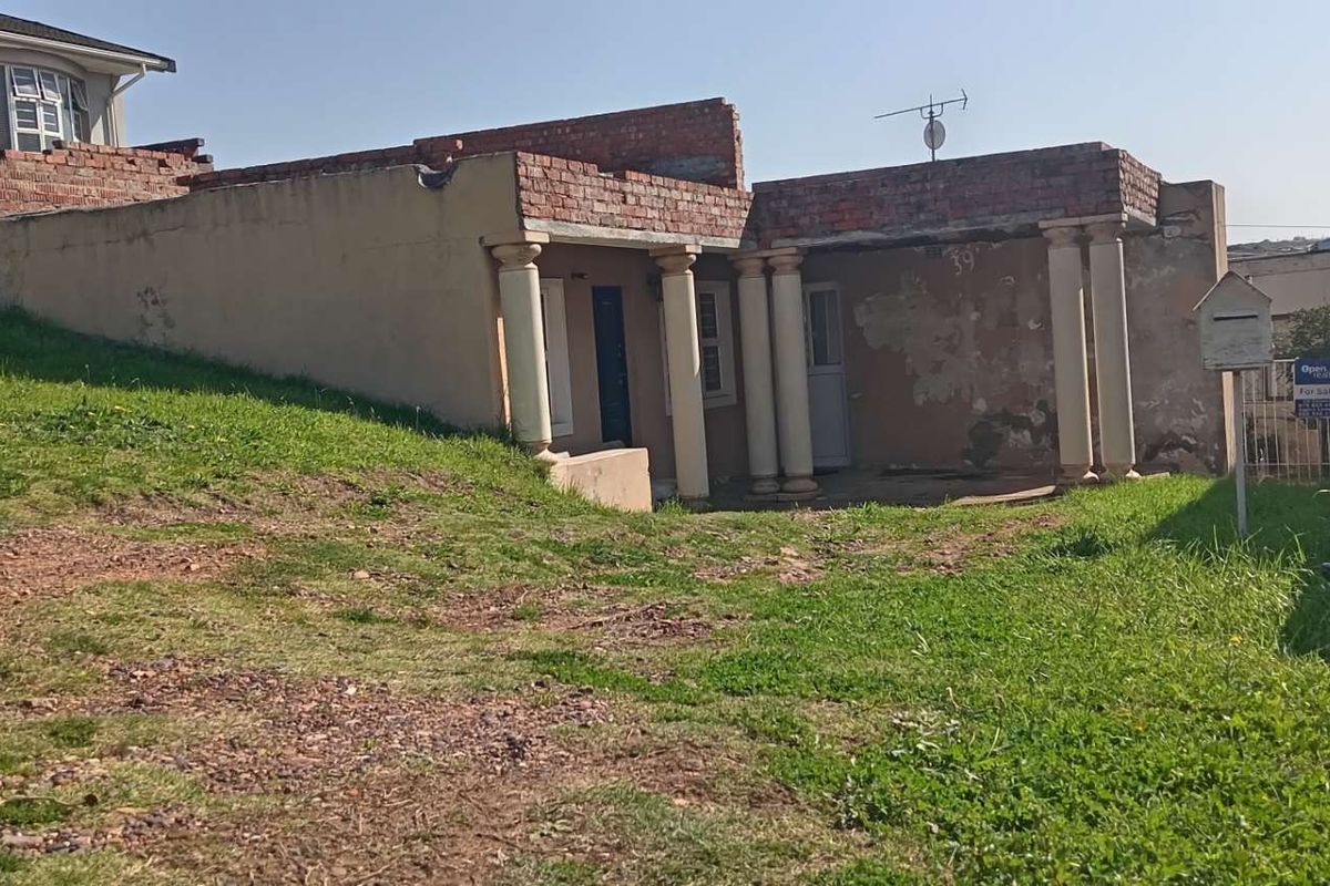 Rear exterior view of the property featuring a covered patio area with columns, showing significant signs of wear and unfinished structural brickwork.