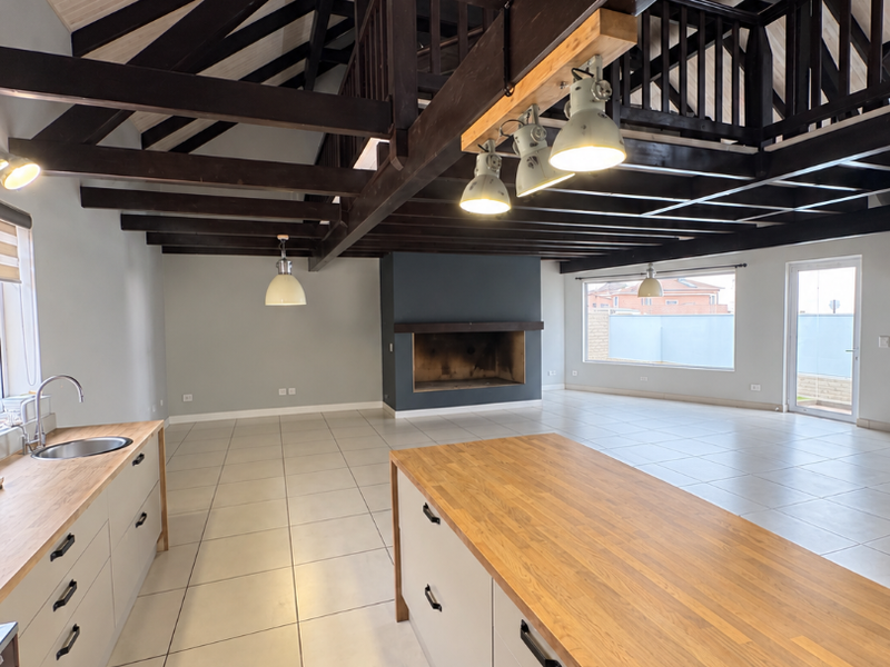 Spacious open-plan living and kitchen area featuring high vaulted ceilings with exposed timber beams, a large kitchen island, and a central built-in fireplace.