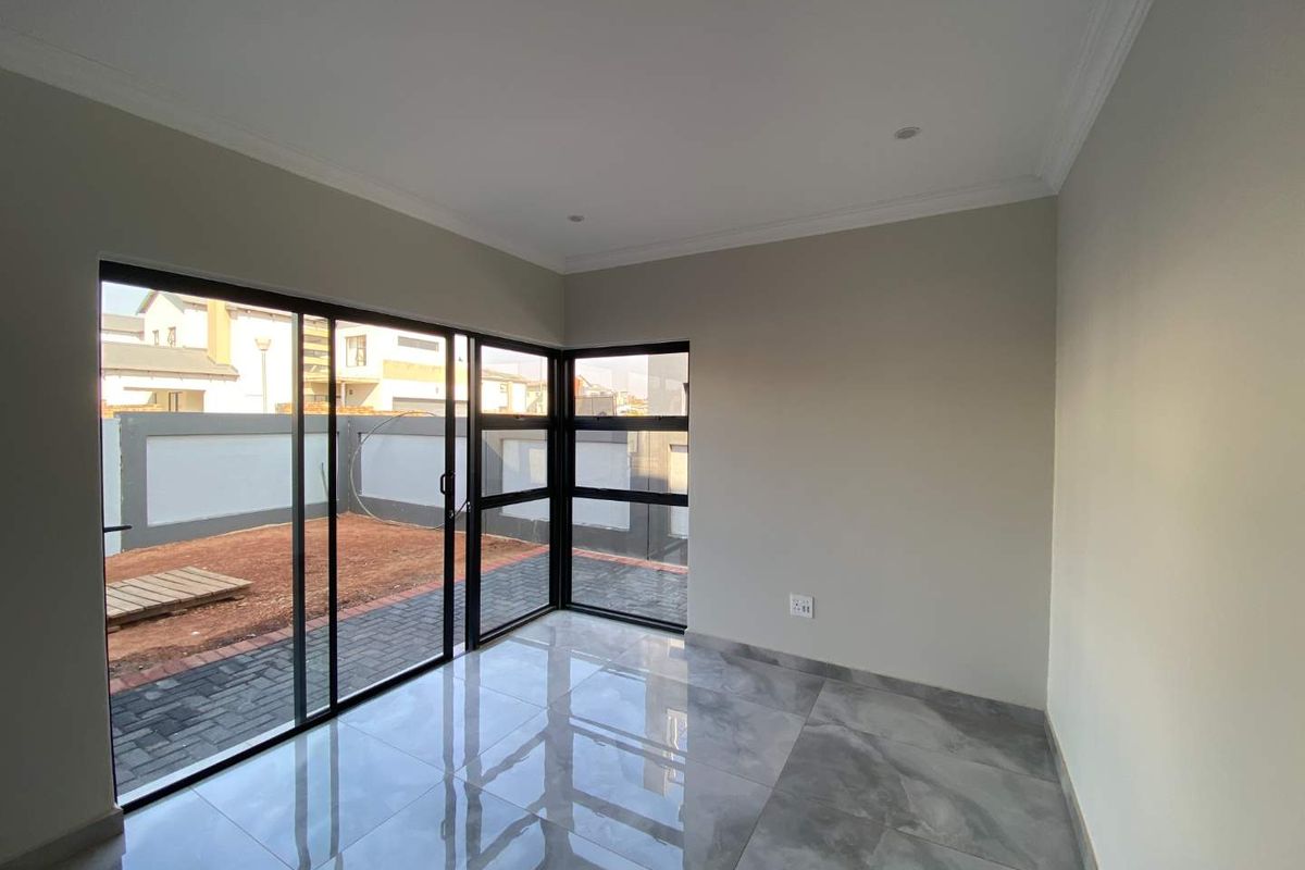 A bright, modern living area featuring large format grey porcelain tiles, black aluminium sliding doors, and a corner window providing access to the rear garden.