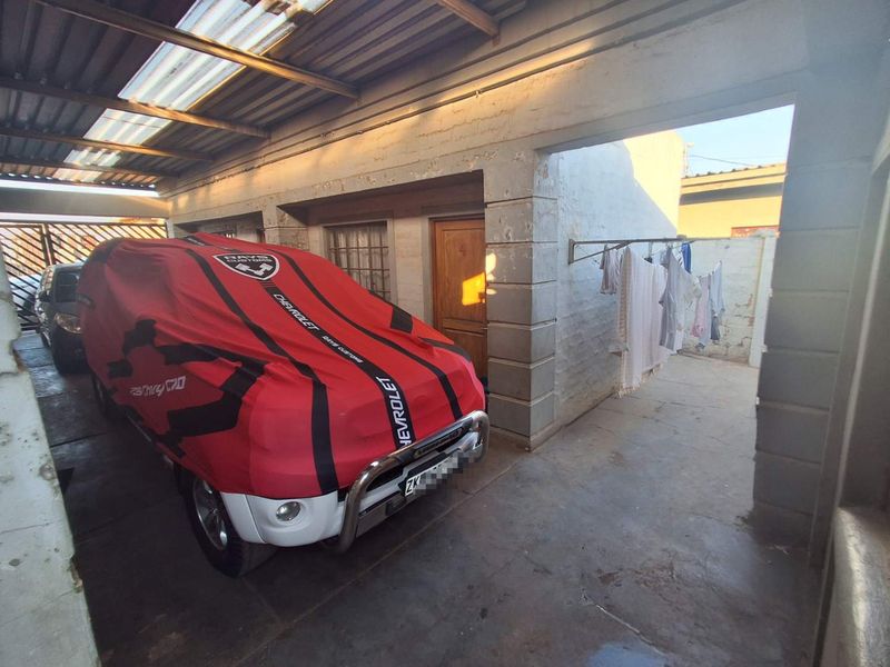 A covered garage area featuring concrete flooring, brick masonry walls, and a corrugated roof structure.