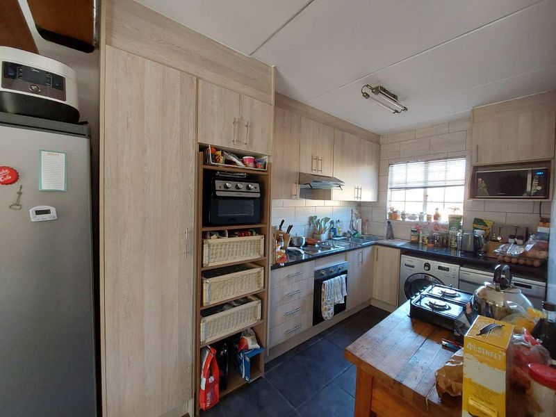 Functional kitchen featuring light wood-finish cabinetry, dark countertops, tiled backsplash, and integrated laundry plumbing, offering a practical layout for daily meal preparation.