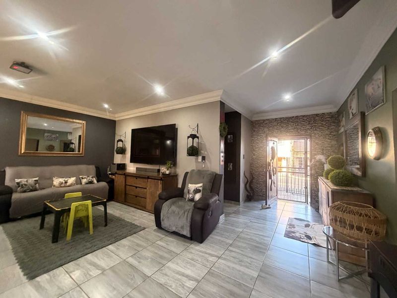 Spacious living room featuring a stone-cladding accent wall, neutral ceramic floor tiles, recessed downlighting, and direct access to the exterior through a security gate.
