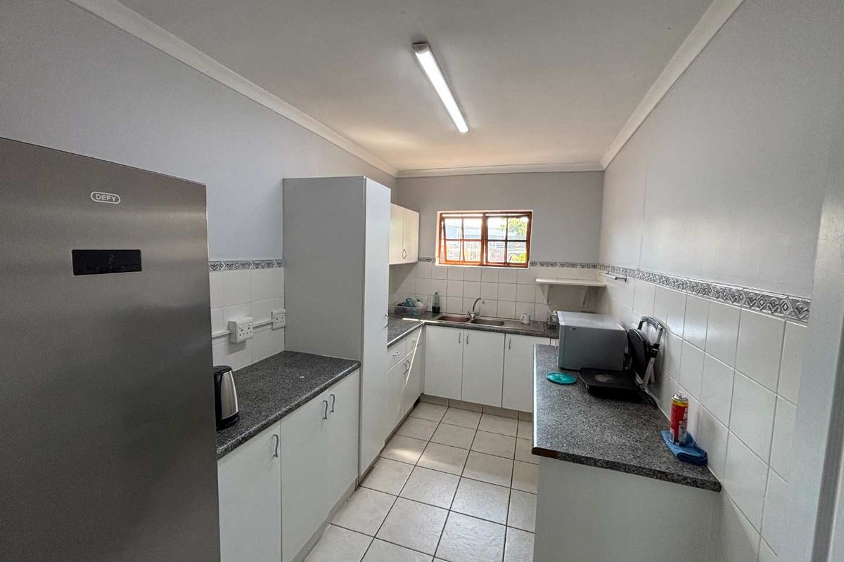 A functional galley-style kitchen featuring tiled flooring, laminate countertops, built-in cabinetry, and a stainless steel sink.