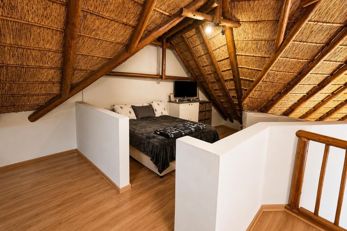 A cozy loft bedroom featuring exposed timber rafters, a traditional thatched roof, and laminate flooring, with half-height partition walls creating a semi-private sleeping area.