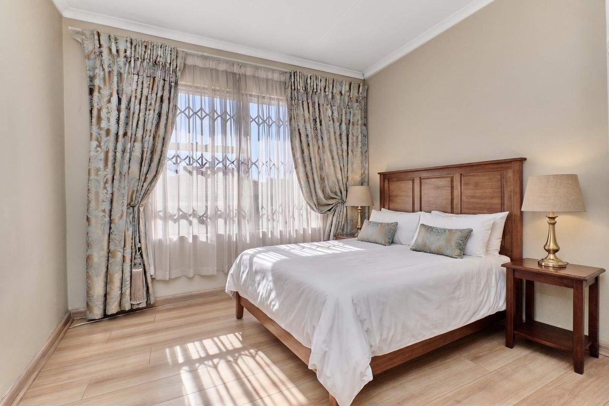 A well-maintained bedroom featuring light-toned laminate flooring, neutral wall finishes, and a large window fitted with a security gate.