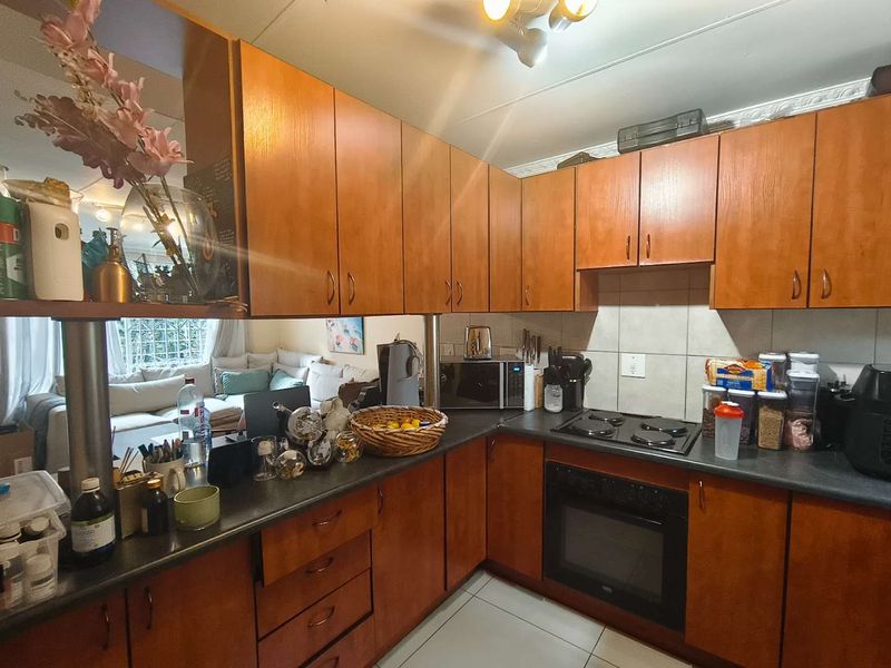 A functional kitchen featuring wood-tone cabinetry, dark laminate countertops, built-in oven, electric hob, and tiled backsplash, opening into the adjacent living area.