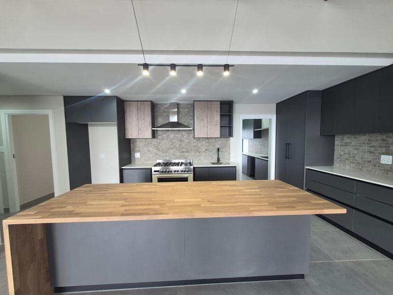 Modern kitchen featuring a large central island, dark cabinetry, stone tile backsplash, and integrated gas stove with stainless steel extractor fan.