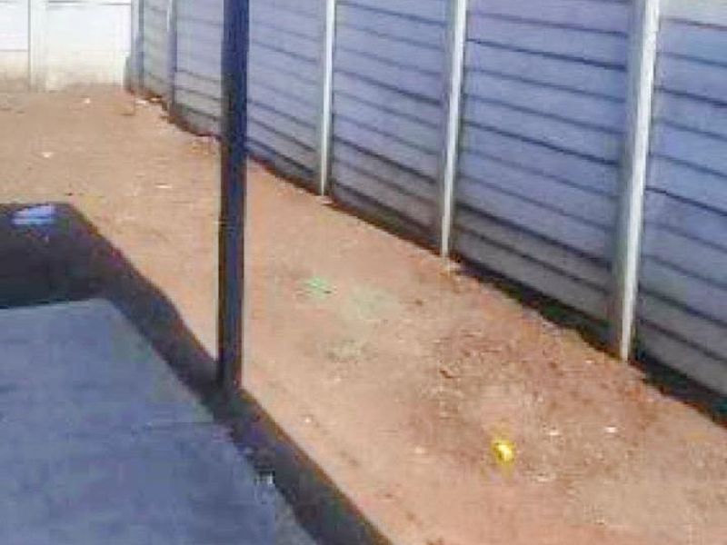 A rear exterior view of the townhouse featuring a paved patio area and a precast concrete boundary wall with unlandscaped ground.