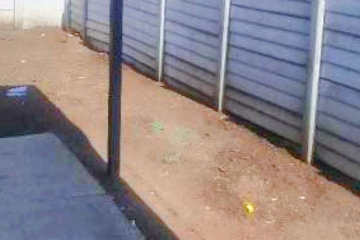 A rear exterior view of the townhouse featuring a paved patio area and a precast concrete boundary wall with unlandscaped ground.