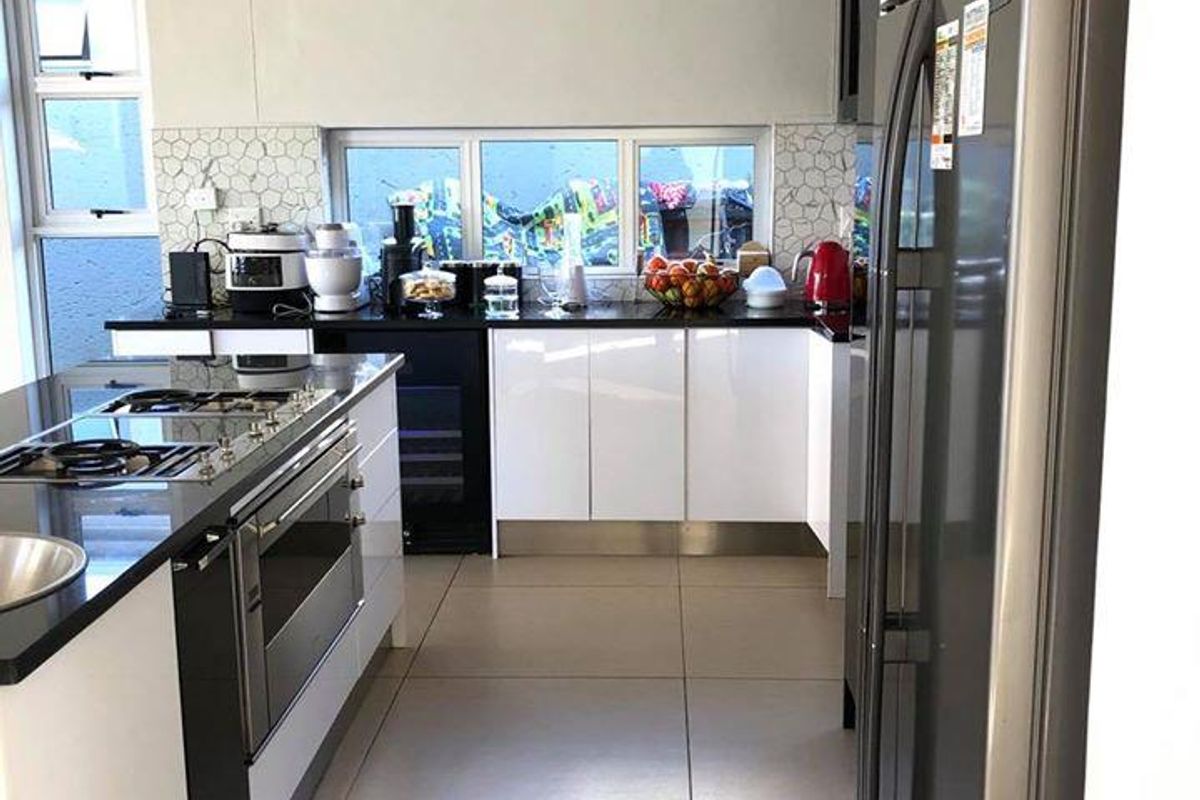 Modern kitchen featuring white cabinetry, dark countertops, integrated gas hob, built-in oven, and large format floor tiles with a tiled backsplash.