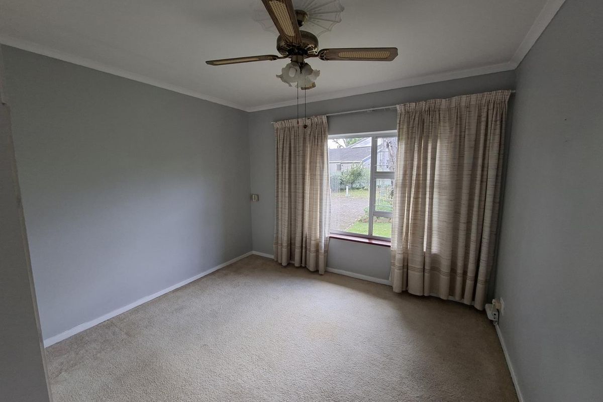 A vacant bedroom featuring neutral grey walls, carpeted flooring, and a ceiling fan, offering a blank canvas for personalization.