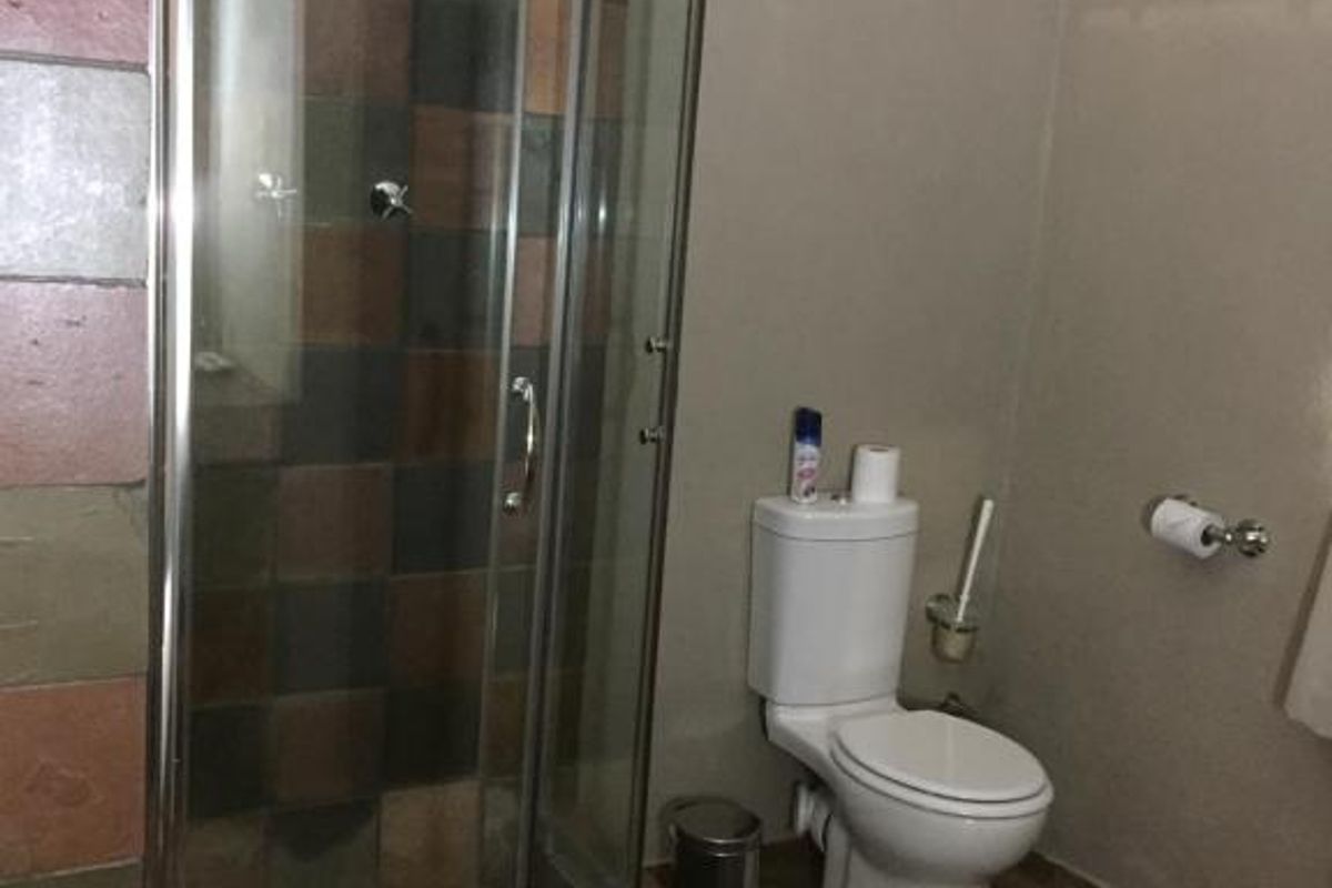 A functional bathroom featuring a glass-enclosed shower with multi-colored tiled walls and matching floor tiles, alongside a standard white toilet.