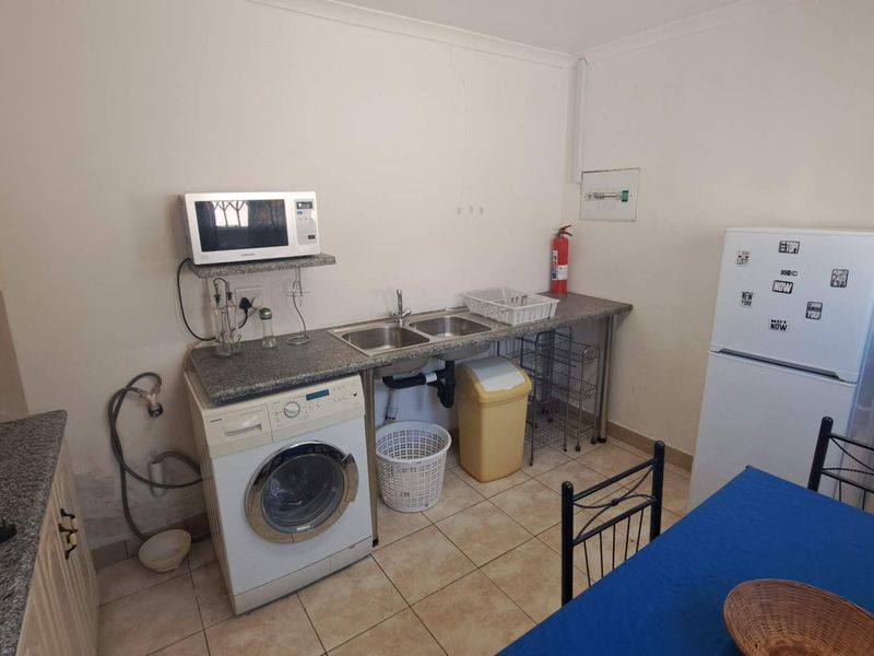 A functional laundry area featuring a double sink, granite countertop, and tiled flooring, with visible wall wear requiring maintenance.