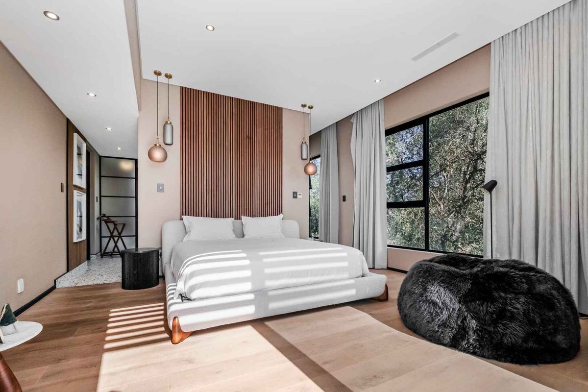 Modern bedroom featuring timber slat feature wall, recessed ceiling lighting, large windows with garden views, and high-quality timber flooring.