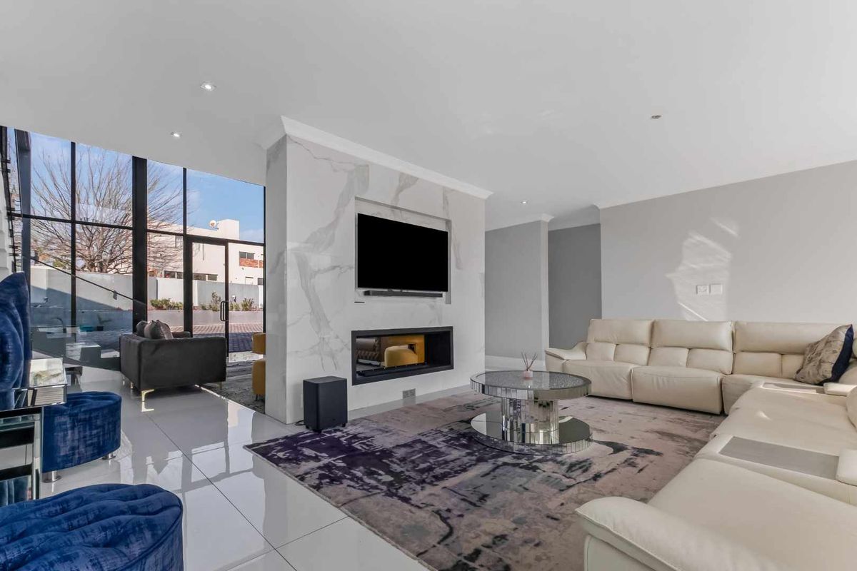 Modern living room featuring a striking marble-clad fireplace wall, large floor-to-ceiling windows, and polished tiled flooring, creating a bright and contemporary atmosphere.