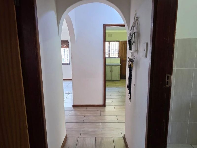 A bright hallway featuring arched architectural details, tiled flooring, and wooden door frames, providing a clear transition between living spaces.